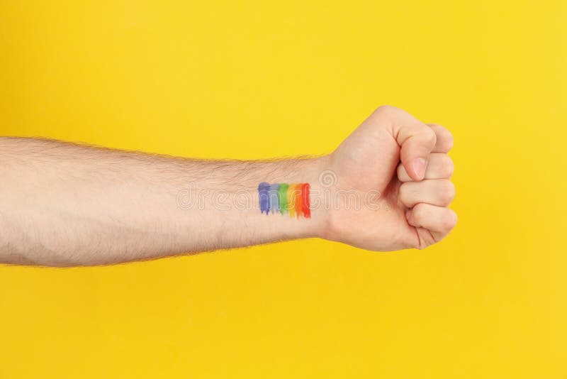Arc-en-ciel mâle lgbt de main sur l'espace jaune d'arrière-plan du texte photos stock