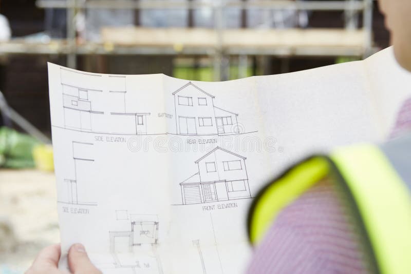 Close Up Of Architect On Building Site Looking At Plans For House