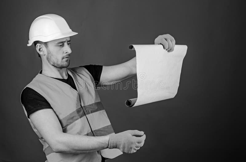 Architect concept. Man in helmet, hard hat holds building plan, controls works, red background. Engineer, architect stock photos Architect concept. Man in helmet, hard hat holds building plan, controls works, red background. Engineer, architect stock photos