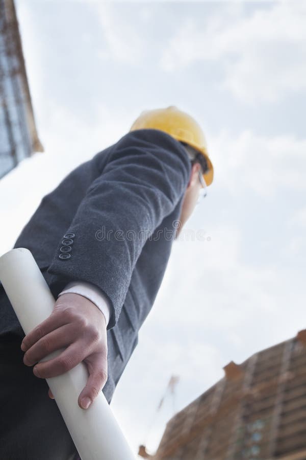 Architect holding blue print and looking up, low angle view stock photo Architect holding blue print and looking up, low angle view stock photo