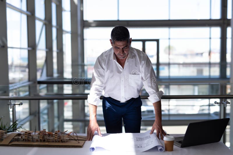 Architect reviewing blueprints at office desk with model and laptop royalty free stock images