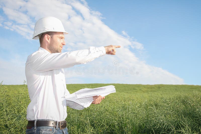 Architecteningenieur die met tekeningen in witte helm aan plaats van bouwwerf richten royalty-vrije stock foto Architecteningenieur die met tekeningen in witte helm aan plaats van bouwwerf richten royalty-vrije stock foto