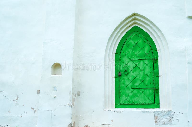 Architecture view of architecture elements - aged bright green metal forged door with arcade on the white stone wall.