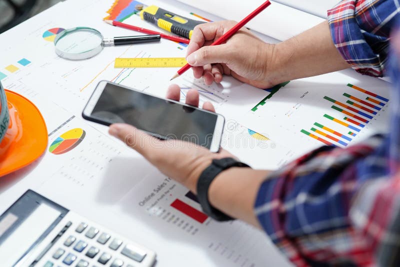 Architetti o ingegneri che lavorano per la contabilità di progetti con grafico, telefono cellulare e strumenti in ufficio immagine stock Architetti o ingegneri che lavorano per la contabilità di progetti con grafico, telefono cellulare e strumenti in ufficio immagine stock
