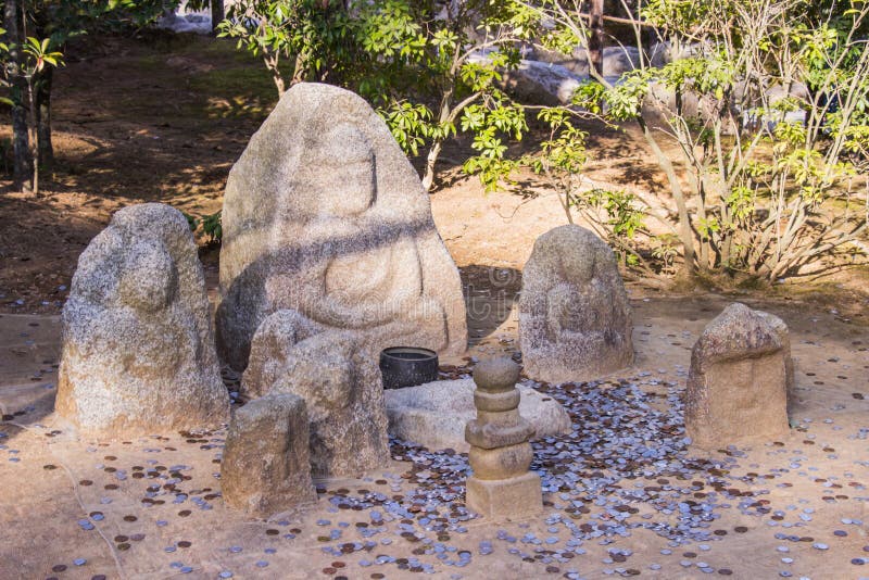 Area at tourists throw coins for pray blessings from stone buddha at carvings inside the garden of Kinkakuji Temple Kyoto, Japan