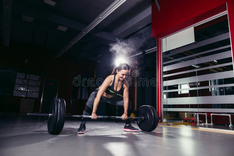Arg passformkvinna i idrottshallen. Muskulös ung konditionkvinna som lyfter en viktcrossfit i idrottshallen Skivstång för konditionkvinnadeadlift Arg passformkvinna Arg passformstil arg passform och kondition