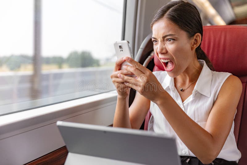 Angry Asian business woman upset screaming at phone call for communication problem or wifi internet connection during commute transport by train or bus. Worker working on laptop yelling mad. Angry Asian business woman upset screaming at phone call for communication problem or wifi internet connection during commute transport by train or bus. Worker working on laptop yelling mad.