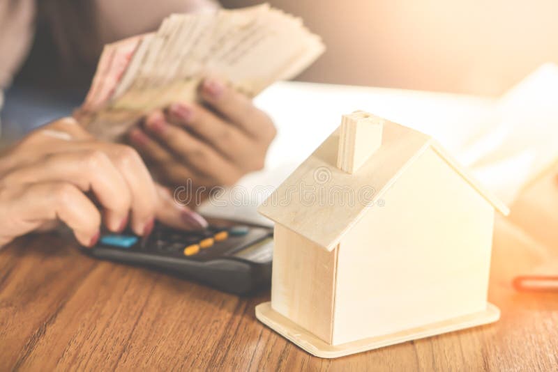 Argent calculateur de main de femme avec le modèle de maison sur la table en bois surfaçant pour acheter ou louer à la maison