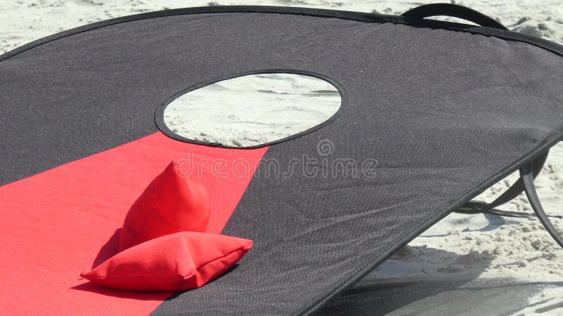 Armação de uma tábua vermelha e preta de milho na areia da praia com sacos de feijão azul e vermelho pousando nela