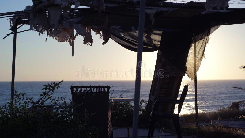 Armchairs and table in abandoned pavilion on coast of Mediterranean sea at sunset. Neglected summerhouse with no people