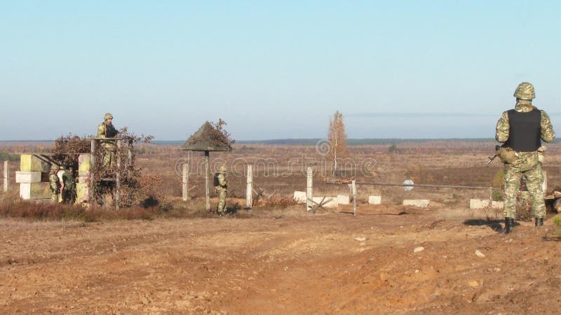 Armed soldiers patrol the territory. A column of vehicles is approaching a protected area.