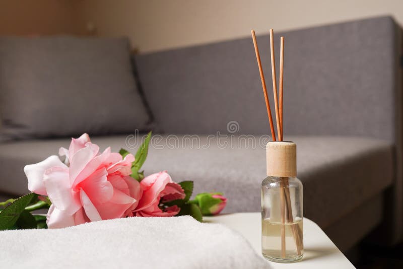 Aroma sticks in glass bottle and brunch of pink roses on commode in living room, close up Handmade reed freshener.