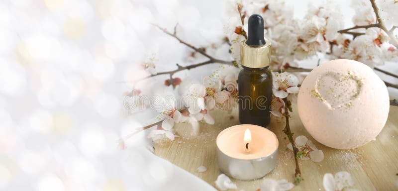 Aromatherapy concept with essential oil bottle, bath bomb, burning candle and blossoms branch.