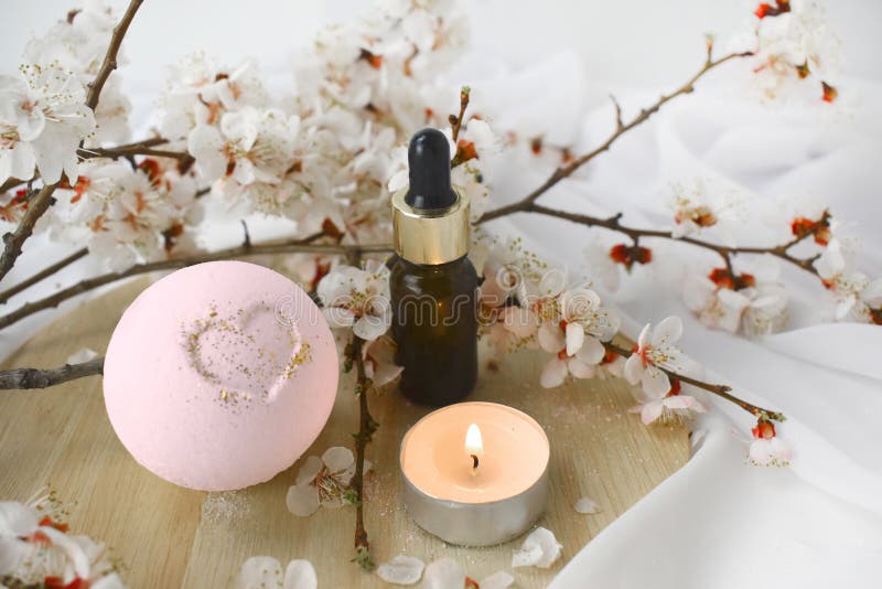 Aromatherapy concept with essential oil bottle, bath bomb, burning candle and blossoms branch.