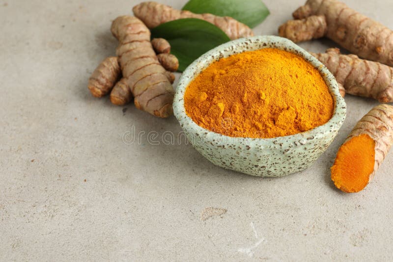 Aromatic turmeric powder in bowl fresh roots and leaves on light grey table closeup space for text stock foto's
