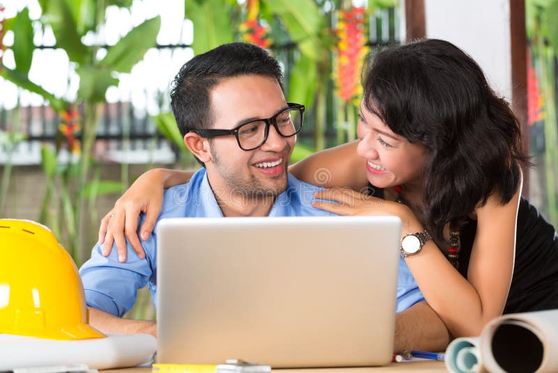 Freelancer - Architect working at home on a design or draft, on his desk are books, a laptop and a helmet or hard hat. Freelancer - Architect working at home on a design or draft, on his desk are books, a laptop and a helmet or hard hat