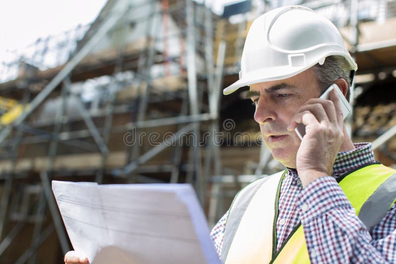 Arquiteto On Building Site que usa o telefone celular imagens de stock royalty free Arquiteto On Building Site que usa o telefone celular imagens de stock royalty free