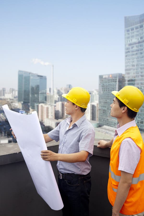 Arquiteto And Construction Worker que fala e que olha o modelo no telhado, cidade no fundo imagem de stock Arquiteto And Construction Worker que fala e que olha o modelo no telhado, cidade no fundo imagem de stock