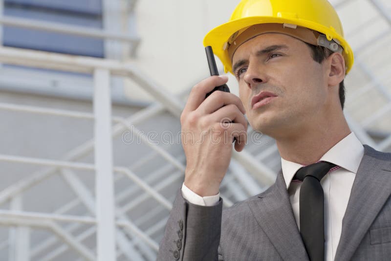 Arquiteto masculino novo que fala no rádio em dois sentidos contra a construção foto de stock Arquiteto masculino novo que fala no rádio em dois sentidos contra a construção foto de stock