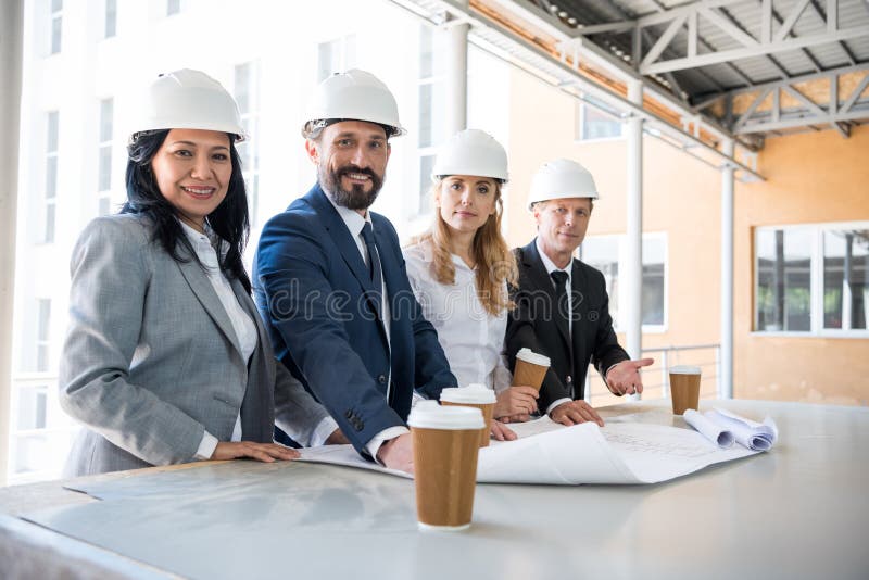 Arquitetos multi-étnicos nos ternos que olham a câmera ao trabalhar com modelos fotos de stock Arquitetos multi-étnicos nos ternos que olham a câmera ao trabalhar com modelos fotos de stock