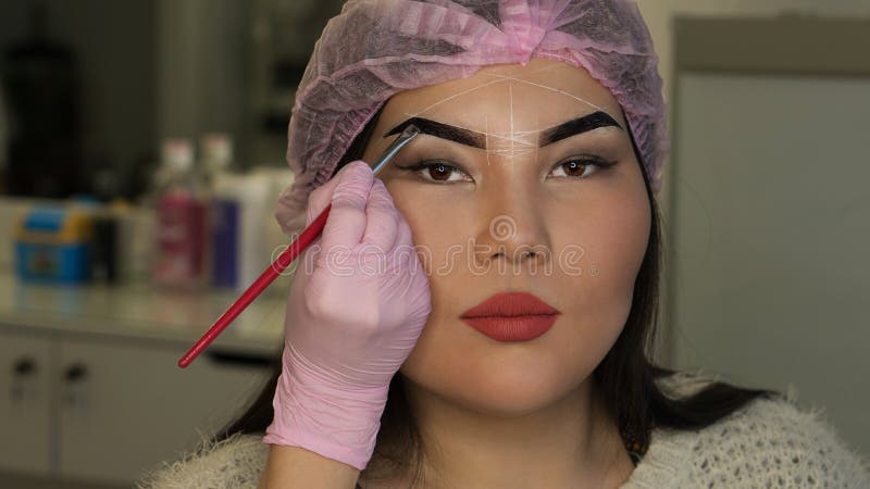 Microbleeding and eyebrow architecture. Beautician applies coloring pigment to girl`s brow, formation of contour. Cosmetic procedure in spa salon. Microbleeding and eyebrow architecture. Beautician applies coloring pigment to girl`s brow, formation of contour. Cosmetic procedure in spa salon