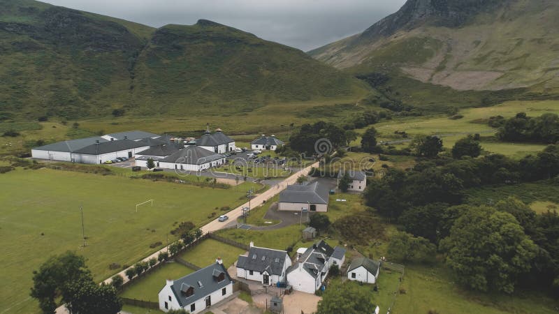 Arran whiskey distillery aerial. Road in green mountains valley. Scottish village with houses, camp