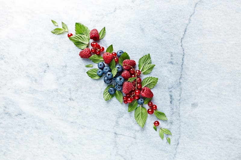 An Arrangement of fresh raspberries, blueberries, red currant and mint leaves on gray marble background.