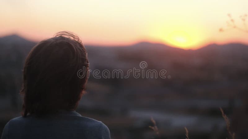 Arrière vue heureux insouciant adolescent garçon d'âge avec le vent souffler dans les cheveux regardant la fin du coucher du solei banque de vidéos
