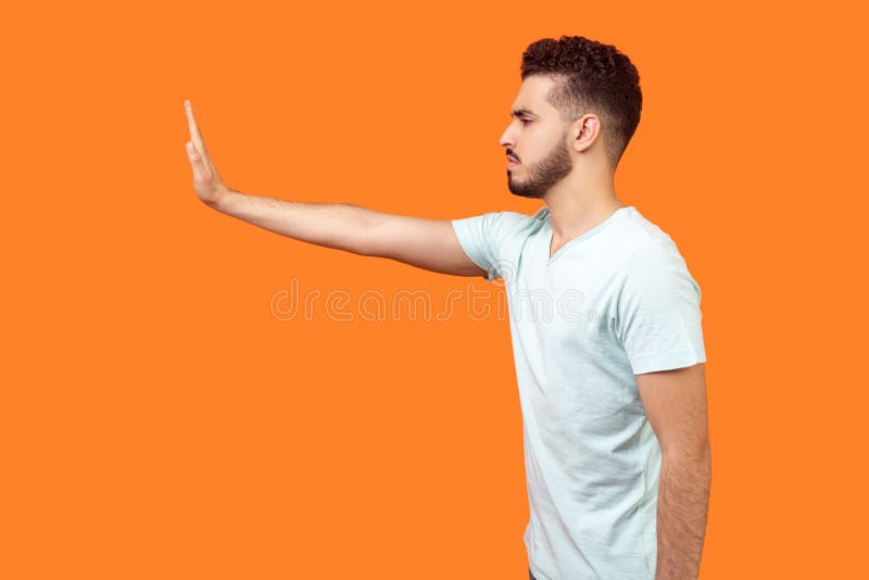 Arrêt! Vue de côté de l'homme autoritaire sérieux brune donnant la main vers la gauche. Photo de studio isolée sur le fond orange photo stock