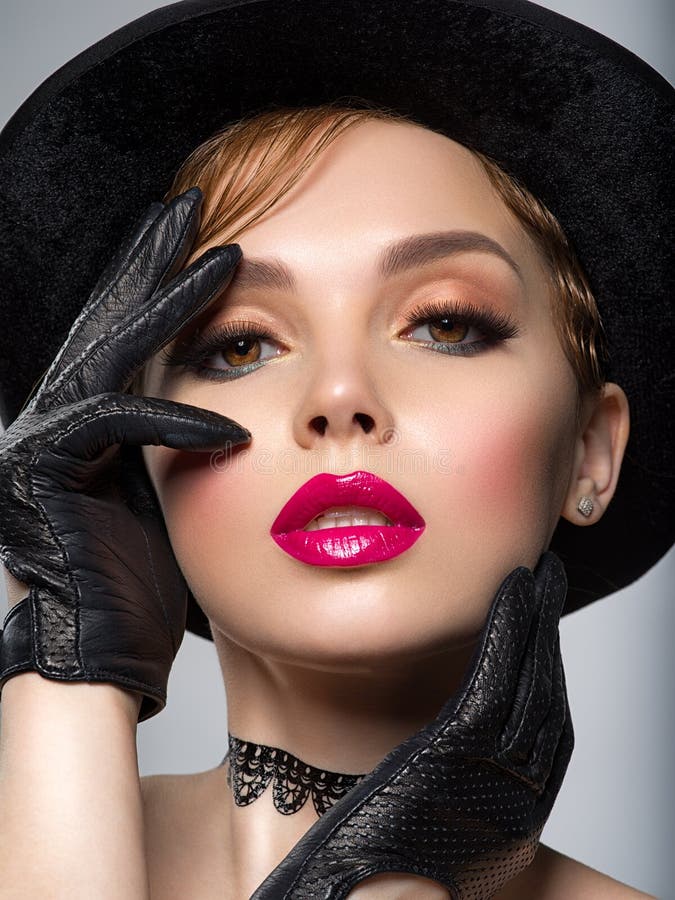 Art portrait of beautiful young woman with orange makeup in a black hat.  Closeup face of a sexy girl with red lipstick on lips.