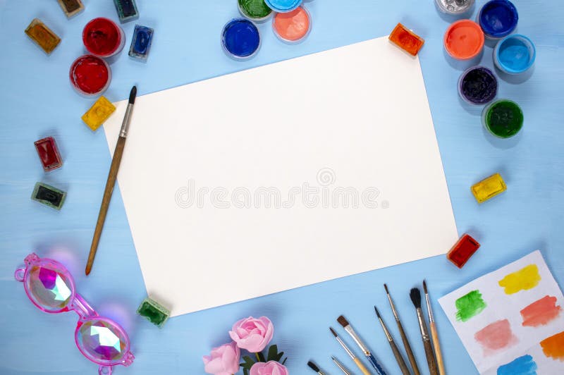 Watercolor, acrylic, brushes and a sheet of paper on a blue background. Flat lay, top view. artist`s table stock photo