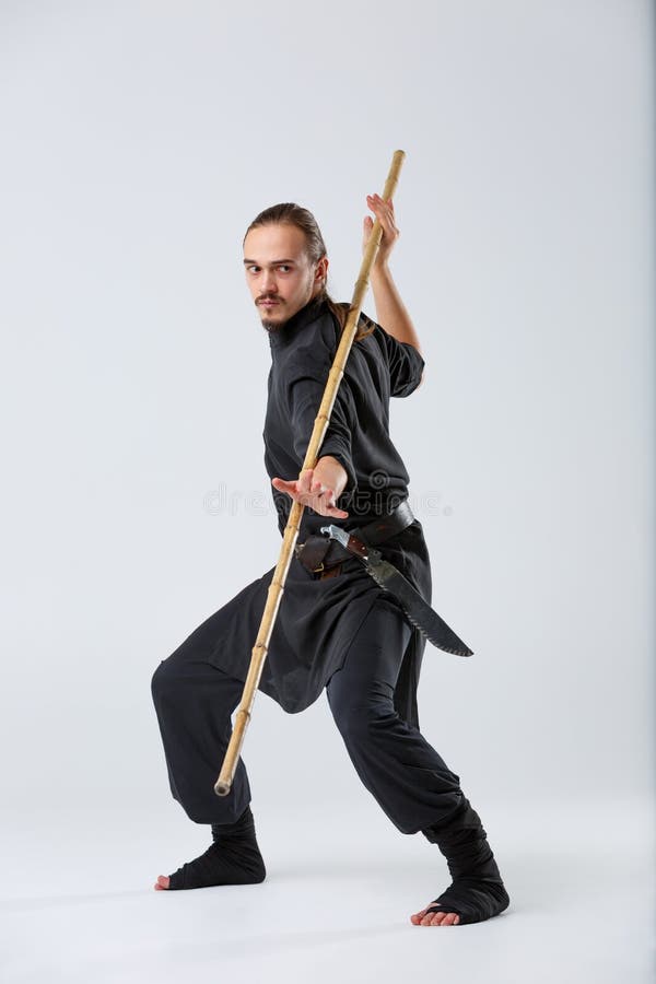 The artful fighter in a black suit, fighting with a long bamboo fighting stick. stock photos The artful fighter in a black suit, fighting with a long bamboo fighting stick. stock photos