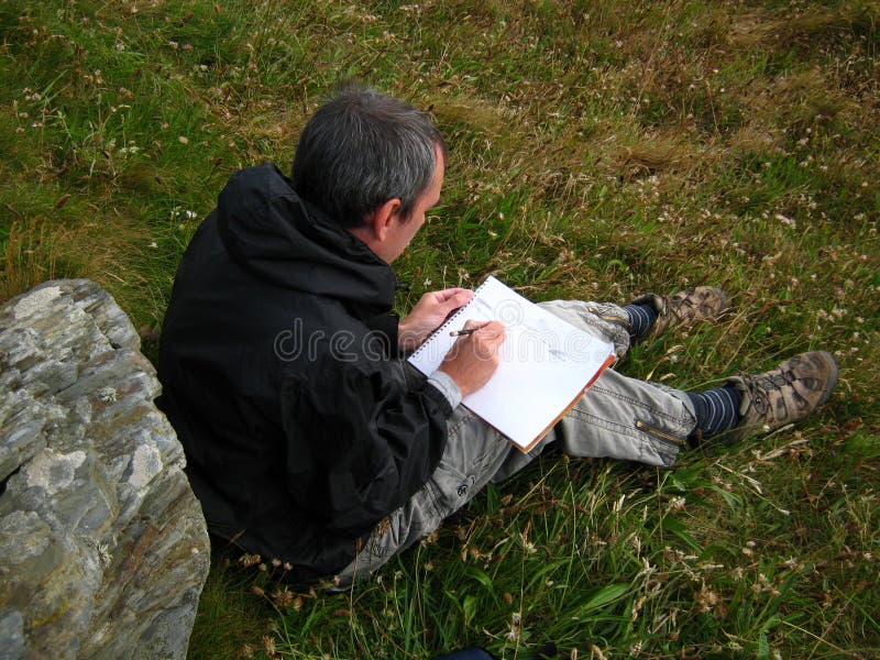 Male artist outside in a field pencil drawing by hand in his sketch pad. Male artist outside in a field pencil drawing by hand in his sketch pad.