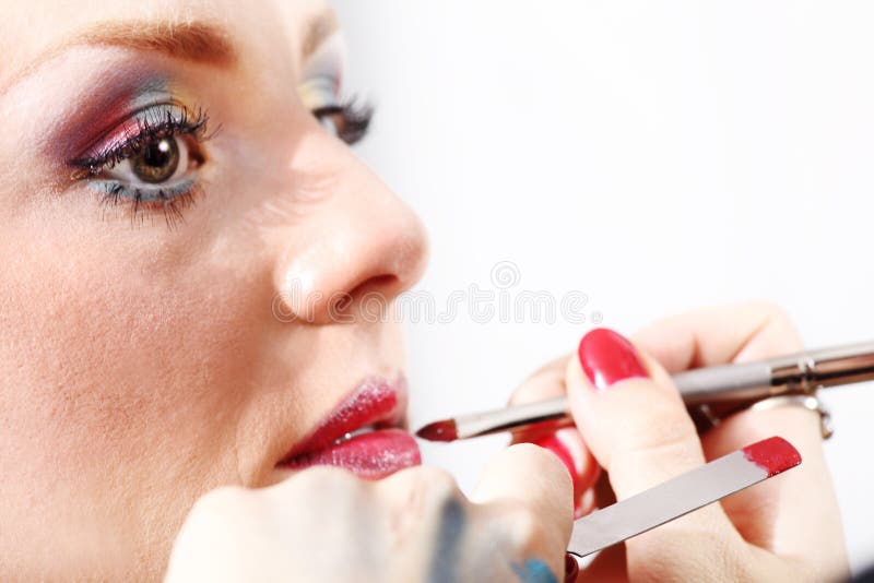 Artista de maquillaje que aplica el lápiz labial en los labios modelo con el cepillo foto de archivo libre de regalías Artista de maquillaje que aplica el lápiz labial en los labios modelo con el cepillo foto de archivo libre de regalías