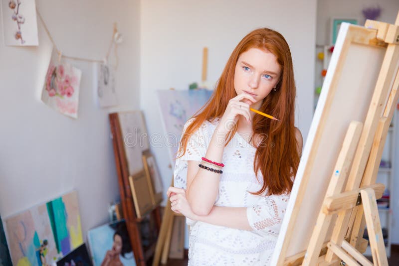 Artista de sexo femenino pensativo atractivo que piensa y que dibuja en lona imágenes de archivo libres de regalías Artista de sexo femenino pensativo atractivo que piensa y que dibuja en lona imágenes de archivo libres de regalías