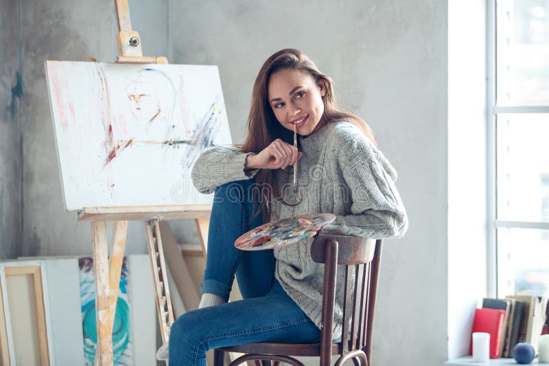 Artista della giovane donna che dipinge a casa il pennello mordace creativo fotografia stock libera da diritti Artista della giovane donna che dipinge a casa il pennello mordace creativo fotografia stock libera da diritti