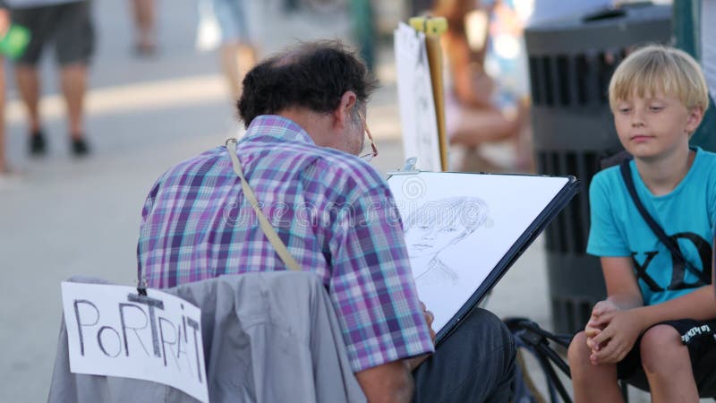 Artiste de rue peint portrait d'un garçon assis sur sa chaise sur le quai au centre-ville