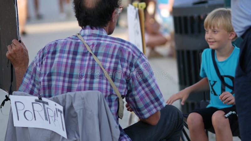 Artiste de rue peint portrait d'un garçon assis sur sa chaise sur le quai au centre-ville