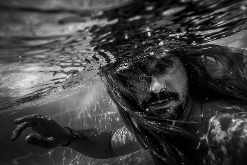 Artistic pic out of focus underwater with long hair man swimming with bubble in water, dark underwater atmosphere with nightmare human abyssal creature like mermaid with beard. Artistic pic out of focus underwater with long hair man swimming with bubble in water, dark underwater atmosphere with nightmare human abyssal creature like mermaid with beard