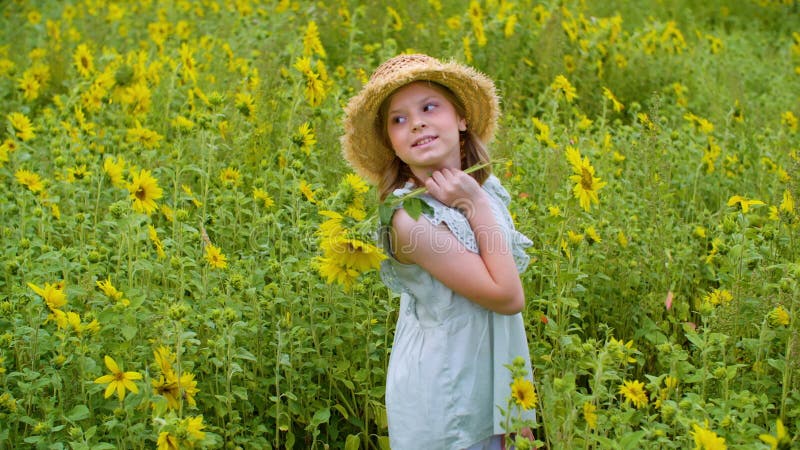 Artistic teenager girl in hat and sunflowers in hands posing on blooming field in countryside. Cute girl standing half