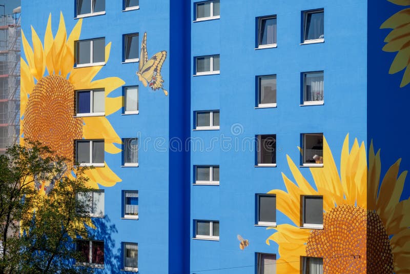 Artistically painted house, skyscraper reaching for the sky, with sunflower blossoms on blue house wall, windows, mural painting