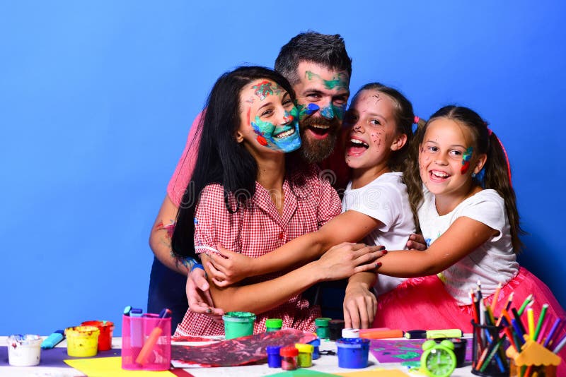 Artists family hugs and smiles. Girls, men and women with cheerful faces by desk with paints. Parents and children painted with gouache on blue background. Family leisure time and art concept. Artists family hugs and smiles. Girls, men and women with cheerful faces by desk with paints. Parents and children painted with gouache on blue background. Family leisure time and art concept