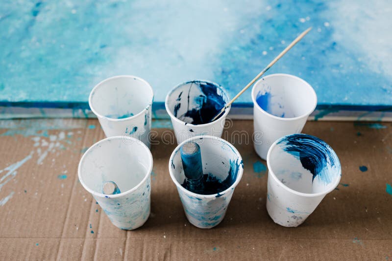 arts and craft hobbies concept, blue and black acrylic painting with colors  in plastic cups and mixed painting tools next to it while the work is in p  Stock Photo - Alamy