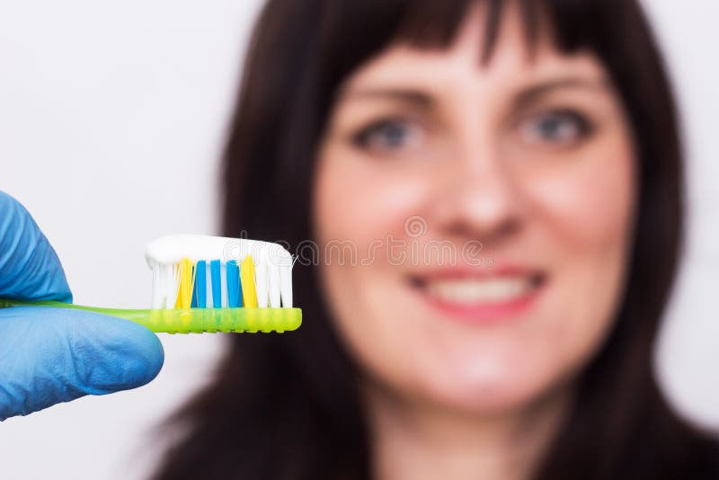 Arts die een tandenborstel met een tandpasta op de achtergrond houden die Kaukasisch meisje met een medische glimlach glimlachen, stock afbeelding Arts die een tandenborstel met een tandpasta op de achtergrond houden die Kaukasisch meisje met een medische glimlach glimlachen, stock afbeelding