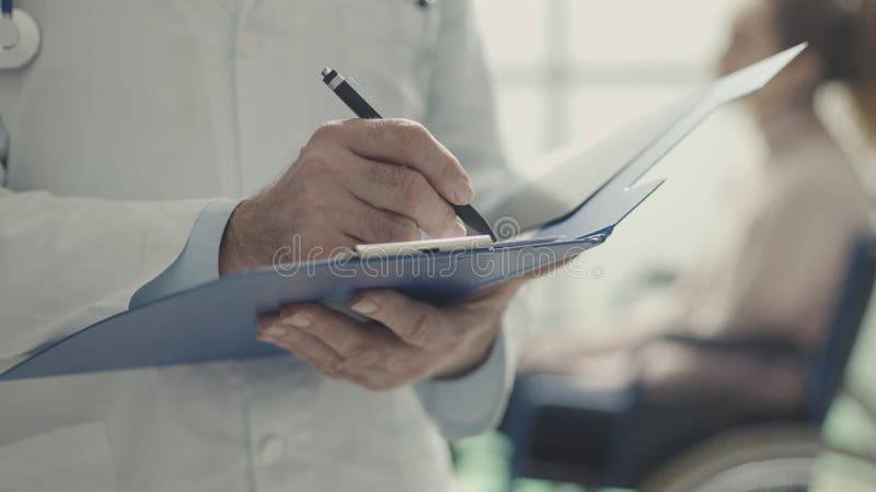 Professional doctor writing medical records and patient in a wheelchair in the background. Professional doctor writing medical records and patient in a wheelchair in the background