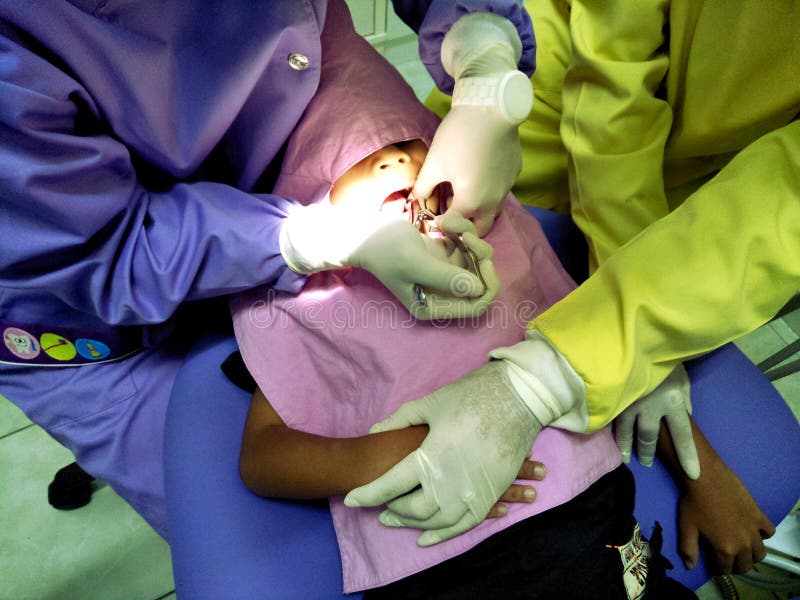 Arts in eenvormig controlerend Tandarts die jong geitje` s tanden onderzoeken bij tandkliniek stock afbeelding Arts in eenvormig controlerend Tandarts die jong geitje` s tanden onderzoeken bij tandkliniek stock afbeelding
