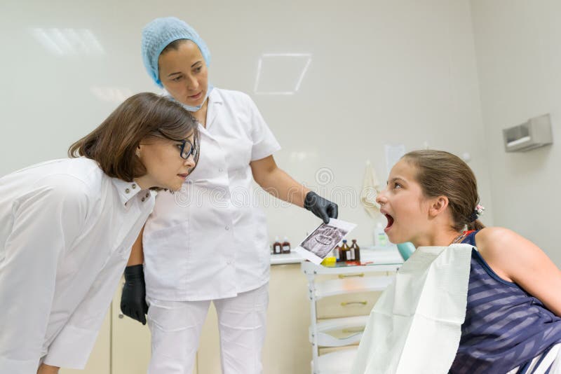 Artsenorthodontists bekijken de röntgenstraal, kindpatiënt in leunstoel Gezondheidszorg, medische en tandheelkundeconcept stock fotografie Artsenorthodontists bekijken de röntgenstraal, kindpatiënt in leunstoel Gezondheidszorg, medische en tandheelkundeconcept stock fotografie
