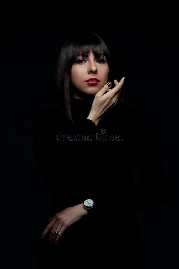 Arty portrait of beautiful dark-haired woman wearing black clothing and luxurious hand watch, posing over dark background. Text-