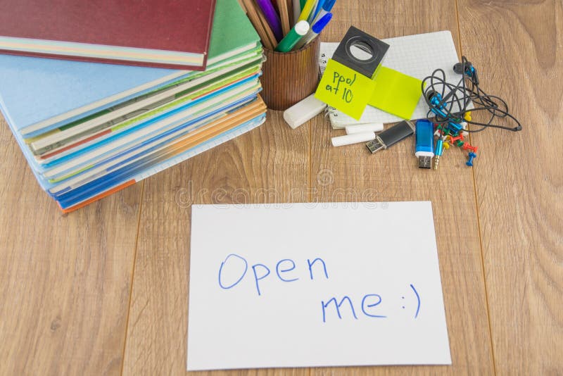 Student desktop,  books, accessories, stationery. in the foreground is an envelope bearing the words ` open me. Student desktop,  books, accessories, stationery. in the foreground is an envelope bearing the words ` open me