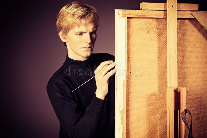 Young man artist paints on canvas with oil paints. Studio shot over black background. Young man artist paints on canvas with oil paints. Studio shot over black background.